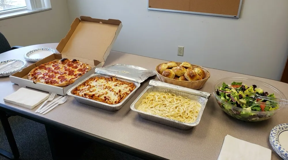 Vito's office catering spread in Alpharetta — foil trays of pasta, fresh pizzas and salads set up for a team lunch